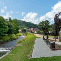 Szczyrk – zagospodarowany bulwar wzdłuż potoku, ścieżka spacerowa i zabudowa apartamentowa na tle gór Beskidu Śląskiego