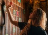 Nastolatka rozwiązuje zagadki w escape roomie — szuka wskazówek na drewnianej ścianie