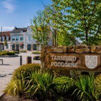 Tarnowo Podgórne – centrum gminy w powiecie poznańskim, tablica z herbem i nazwą miejscowości na tle zadbowanego placu
